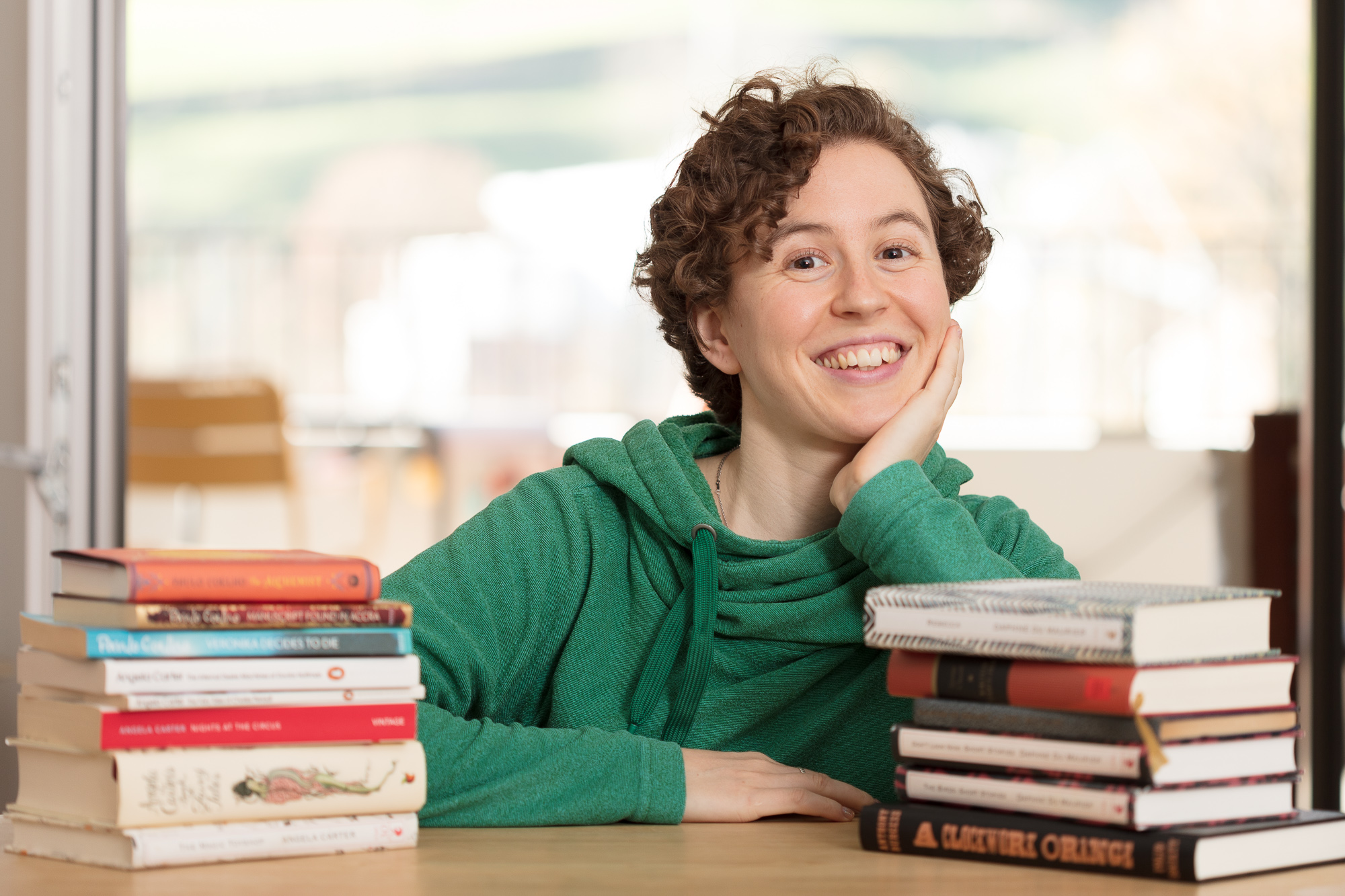The author, a young white woman with short curly hair, posing awkwardly behind 2 small piles of books